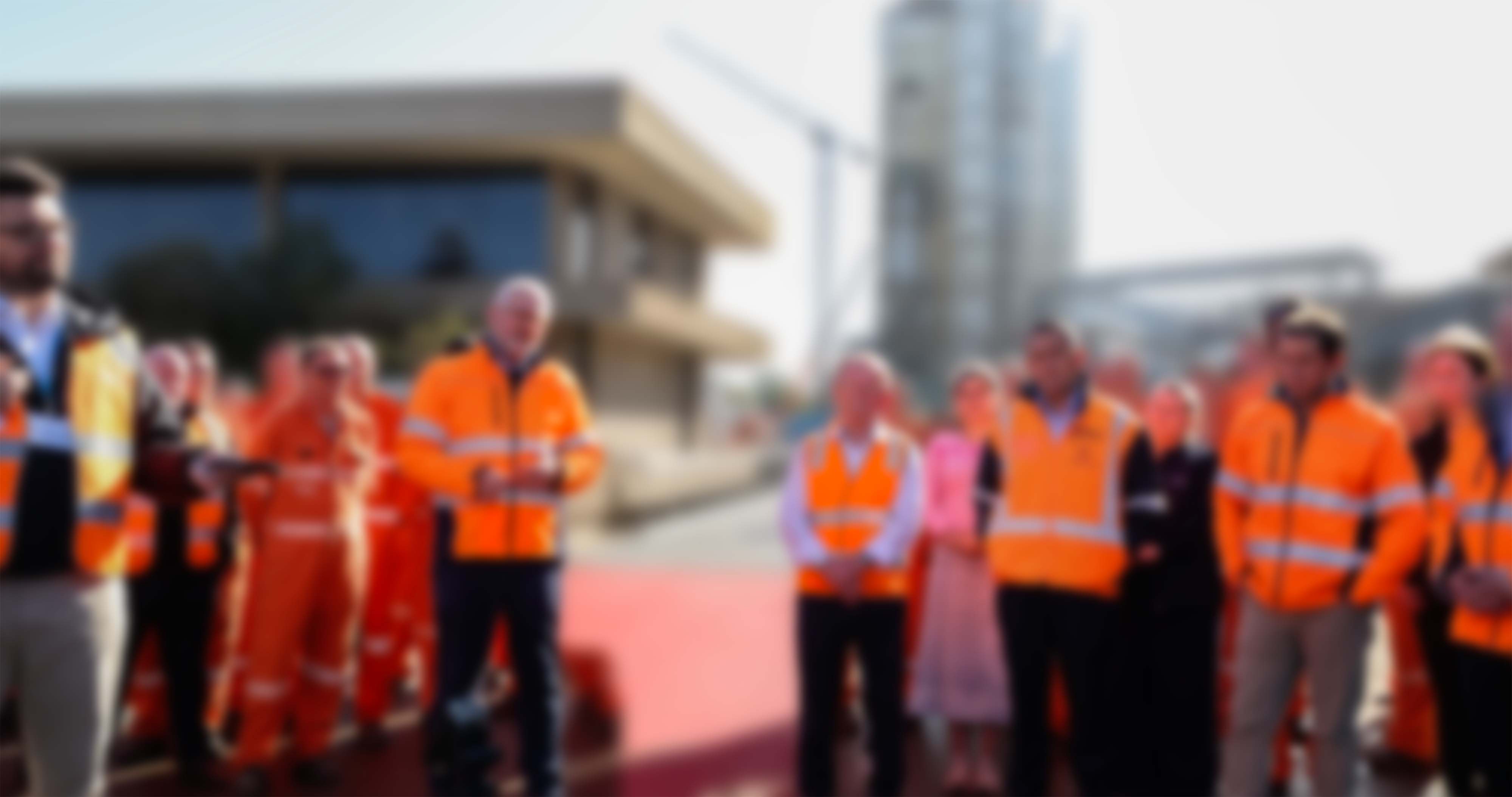 Soft-focus group of workers in high-vis vests posed in front of an industrial facility